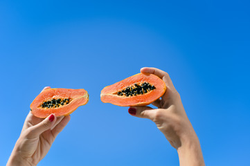 Close up on person hand holding a half papaya fruit on sunny blue sky background