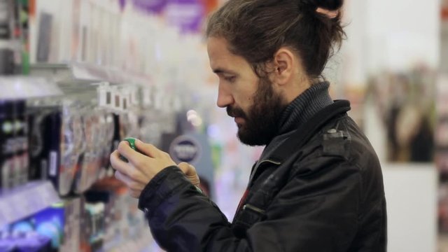 Men with beard and long hair selecting antiperspirant in supermarket.