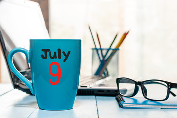 July 9th. Day 9 of month, color calendar on morning coffee cup at business workplace background. Summer concept. Empty space for text