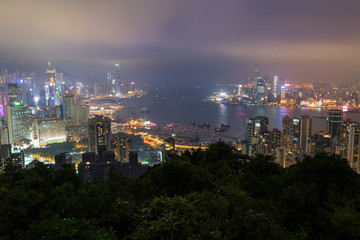 Obraz premium Oświetlone wieżowce i inne budynki na wyspie Hong Kong i Kowloon w Hong Kongu, Chiny. Oglądany ze wzgórza Braemar w mglisty i pochmurny wieczór.