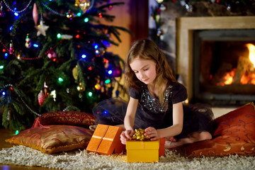 Happy girl opening Christmas gifts by a fireplace