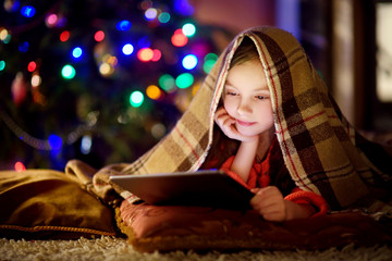 Adorable little girl using a tablet pc by a fireplace on Christmas evening