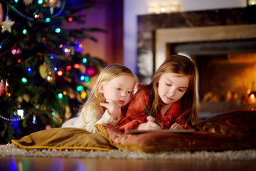 Fototapeta na wymiar Two cute little sisters writing a letter to Santa by a fireplace on Christmas