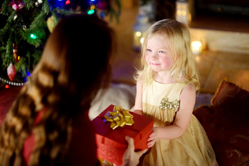 Happy little girl getting a Christmas gift from her mommy
