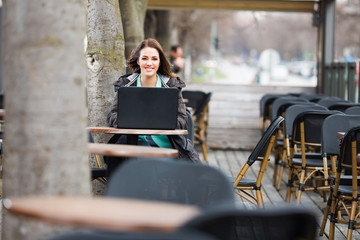 Young woman sitting outside in coffee shop and using her laptop