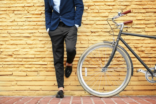 Young businessman with bicycle on yellow brick wall background