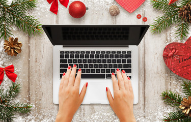 Woman work on laptop. Christmas scene with decorations, tree and gift. Blank screen for mockup. Top...