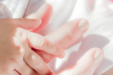 Hand of a caucasian baby on high key held up by the mother