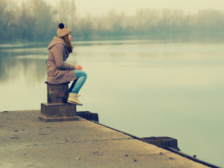 Lonely sad teenage girl sitting on the dock in autumn
