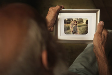 Elderly man holding photo frame with picture of young couple. Happy memories concept.