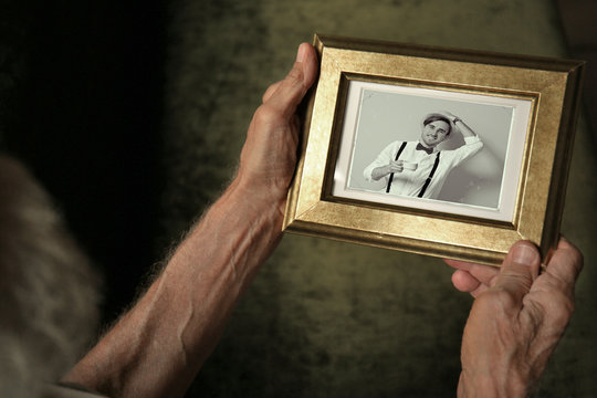 Elderly man holding photo frame with picture of grandson. Happy memories concept.