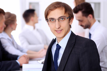 Portrait of cheerful smiling businessman  against a group of  people at meeting.