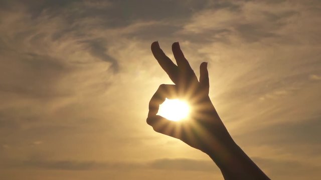 CLOSE UP, DOF: Connecting thumb and index finger in circle over shining sunshine