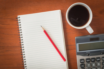 Note book with pencil and a cup of coffee on wood table