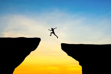 Foto op Plexiglas Man jump through the gap between hill.man jumping over cliff on sunset background,Business concept idea © PThira89