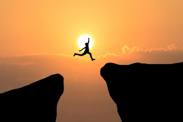 Man jump through the gap between hill.man jumping over cliff on sunset background,Business concept...