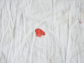 Red period spot on white bed sheet. Period stain is hard to be cleaned. Need to use hot water to...
