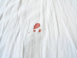 Red period spot on white bed sheet. Period stain is hard to be cleaned. Need to use hot water to...