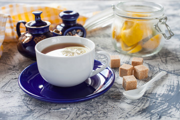tea with a lemon in a cup, a teapot and sugar on a table, selective focus