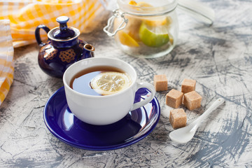 tea with a lemon in a cup, a teapot and sugar on a table, selective focus