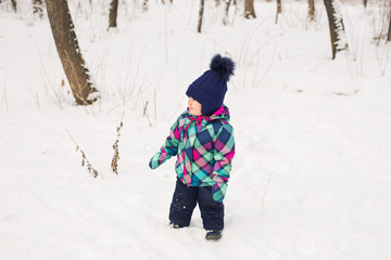 Little girl in winter clothes in snow forest at snowflakes background