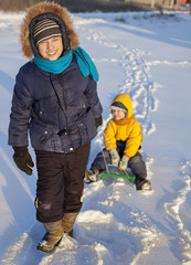 Fototapeta na wymiar Happy Boy pulling sled with his friend on snowy road