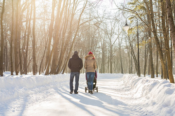 Happy young family walking in the park in winter. The parents carry the baby in a stroller through the snow.