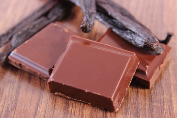 Dark chocolate and fragrant vanilla sticks on wooden surface plank