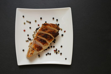 Baked chicken breast with red and black pepper on a white plate on a black background