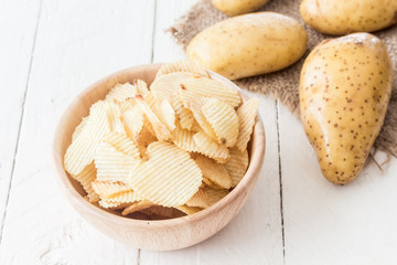 Crispy potato chips in a wooden bowl on wooden table