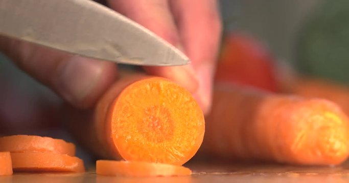 Carrots being sliced on wooden chopping board using sharp kitchen knife. Filmed Macro  in slow motion