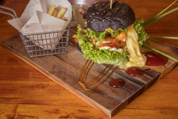 Closeup of beautifully served black burger with French fries isolated on wooden cutting board