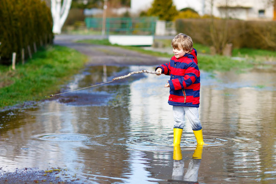 Little kid boy playing with fishing rod by puddle