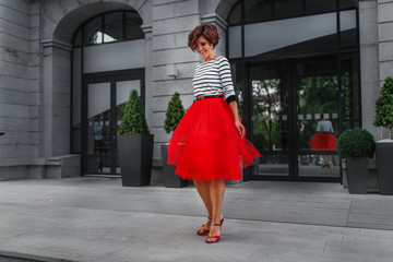 Happy and smiling girl spinning in her red dress on a stairs. Happiness and good mood concept
