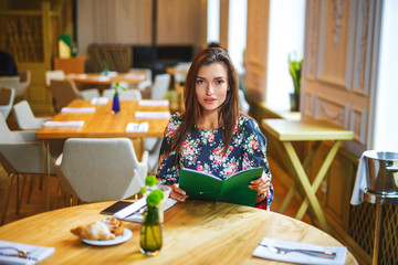 beautiful woman making the order in restaurant. Girl holds in the hands of the menu. She is dressed...