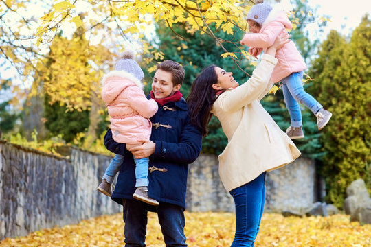 Happy family in autumn park. Parents playing with their daughter on nature on a background of yellow leaves.