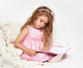 girl child rad book in bed, dressed in pink