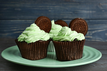 Plate with tasty cupcakes and chocolate cookies on wooden table, close up view
