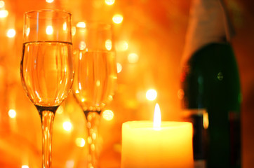 Bright yellow Christmas greetings card or New Years Eve celebration background with an elegant arrangement with flutes and bottle of champagne and burning candles. Bokeh light garland backdrops.