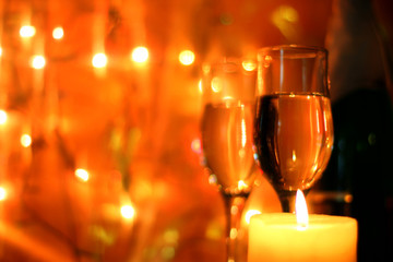 Dark colorful style Christmas greetings or New Years Eve celebration background with an elegant arrangement with flutes and bottle of champagne and burning candles. Bokeh light garland backdrops.