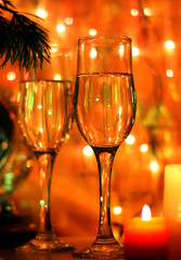 New Years Eve celebration background with an elegant arrangement with flutes and bottle of champagne and burning candles. Bokeh light garland backdrops.