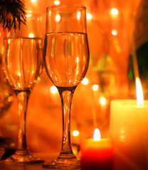 New Years Eve celebration background with an elegant arrangement with flutes and bottle of champagne and burning candles. Bokeh light garland backdrops.