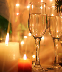 New Years Eve celebration background with an elegant arrangement with flutes and bottle of champagne and burning candles. Bokeh light garland backdrops.