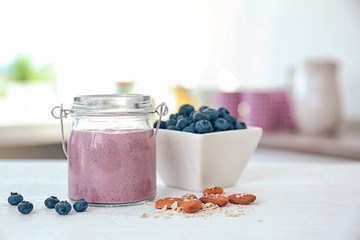 Jar with fresh blueberry smoothie and berries on kitchen table