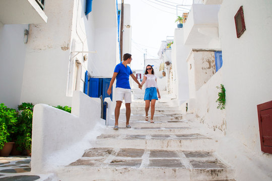 Family Vacation In Europe. Happy Couple At Street Of Typical Greek Traditional Village On Mykonos Island, In Greece