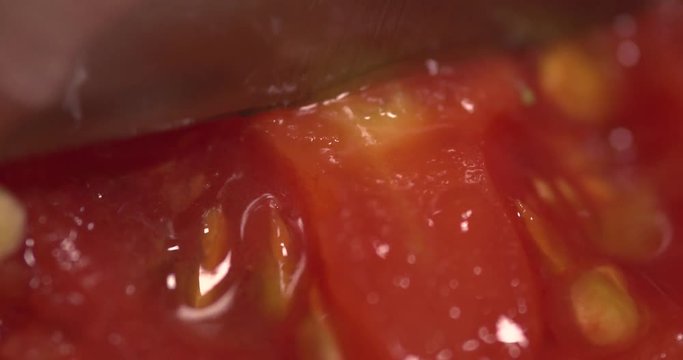 Chef slicing a tomato in extreme closeup. Slow motion footage.