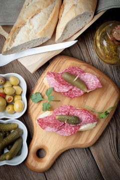 Tapas with sliced salami, olives and cucumber on a wooden table.