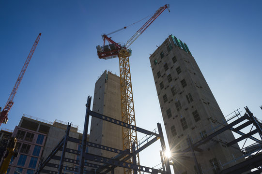Modern hi-rise towers construction site with cranes backlit by morning sun under bright blue sky