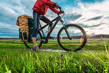 Hiker with loaded bicycle on a green summer meadow