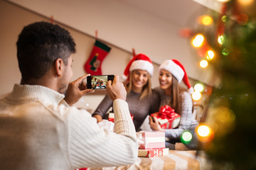 Guy taking a photo of two beautiful girls posing with Christmas gifts.